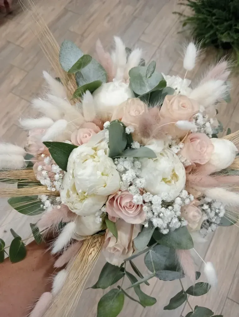 Delicato bouquet da sposa dai colori pastello con rose color crema, peonie bianche, erba della pampa e fogliame di eucalipto.
