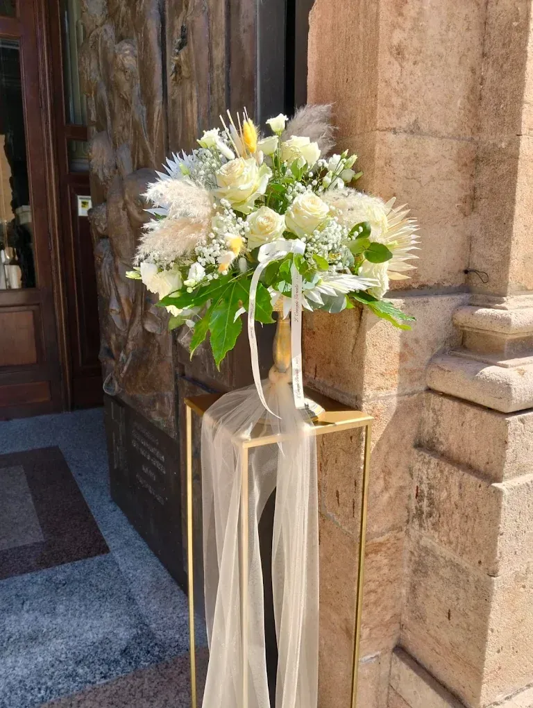 Composizione floreale bianca con nastri su un supporto accanto all'ingresso di un edificio in pietra.