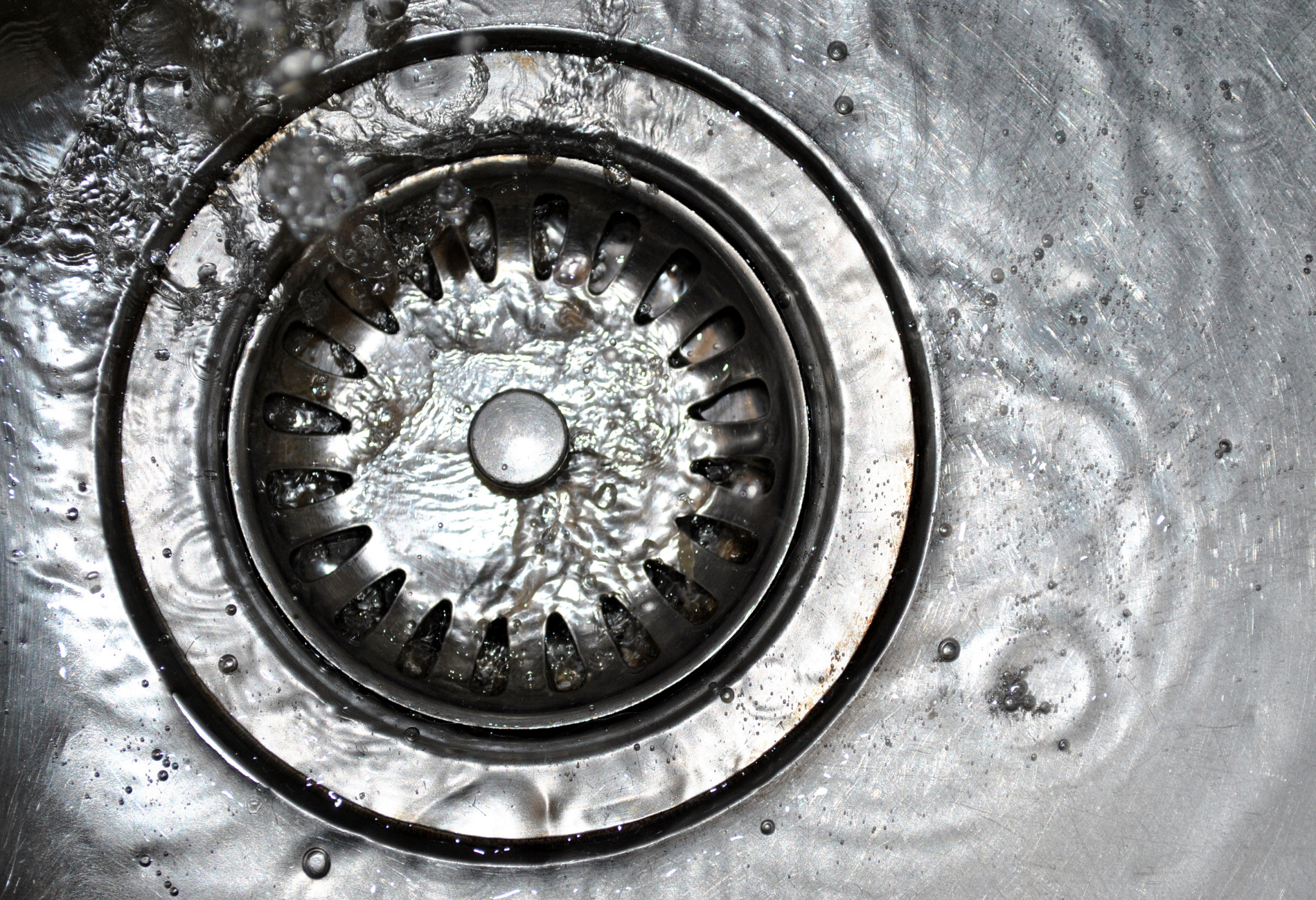 Water flowing into a stainless steel sink drain.