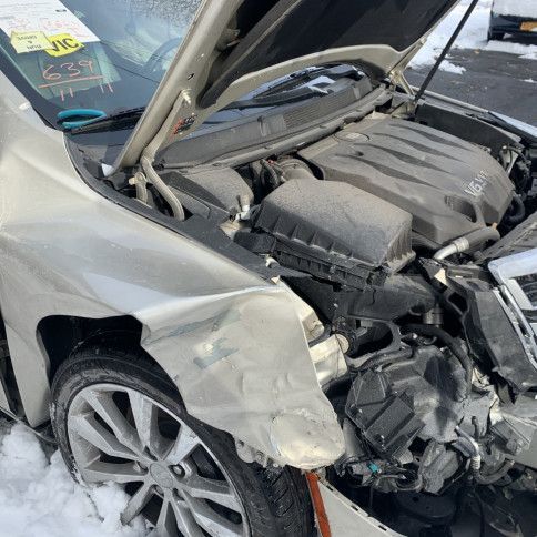 A damaged car with the hood open is parked in the snow.