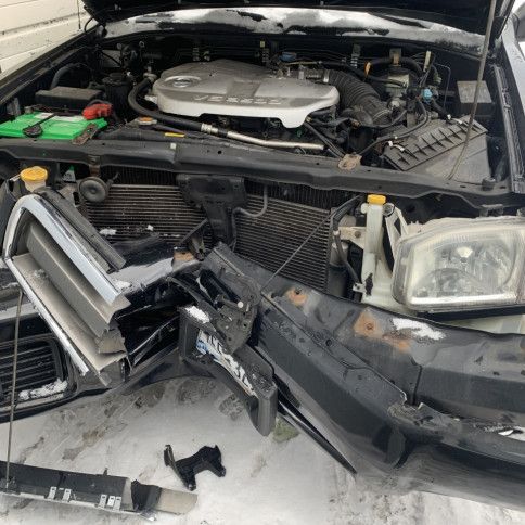 A damaged car with the hood open is sitting in the snow.