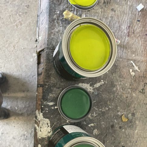 Three cans of green paint are lined up on a table
