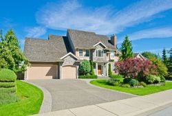 Suburban house with a two-car garage, curved driveway, and landscaped front yard under a blue sky
