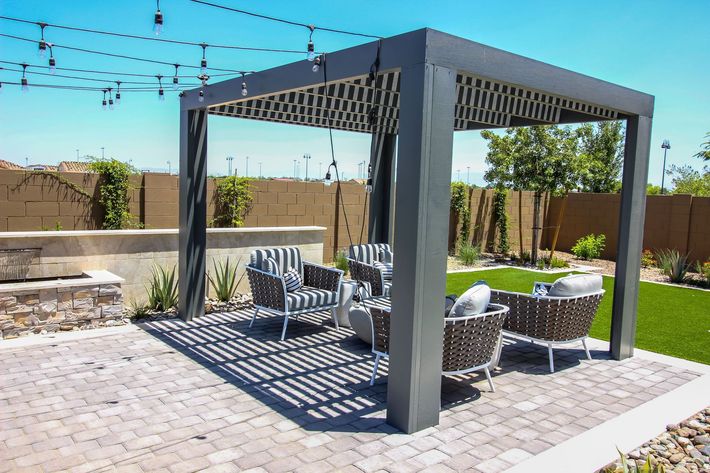 Modern backyard patio with gray pergola, string lights, striped chairs, and outdoor seating area
