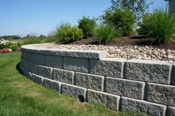 Stone retaining wall with gravel landscaping and green shrubs on a sunny lawn