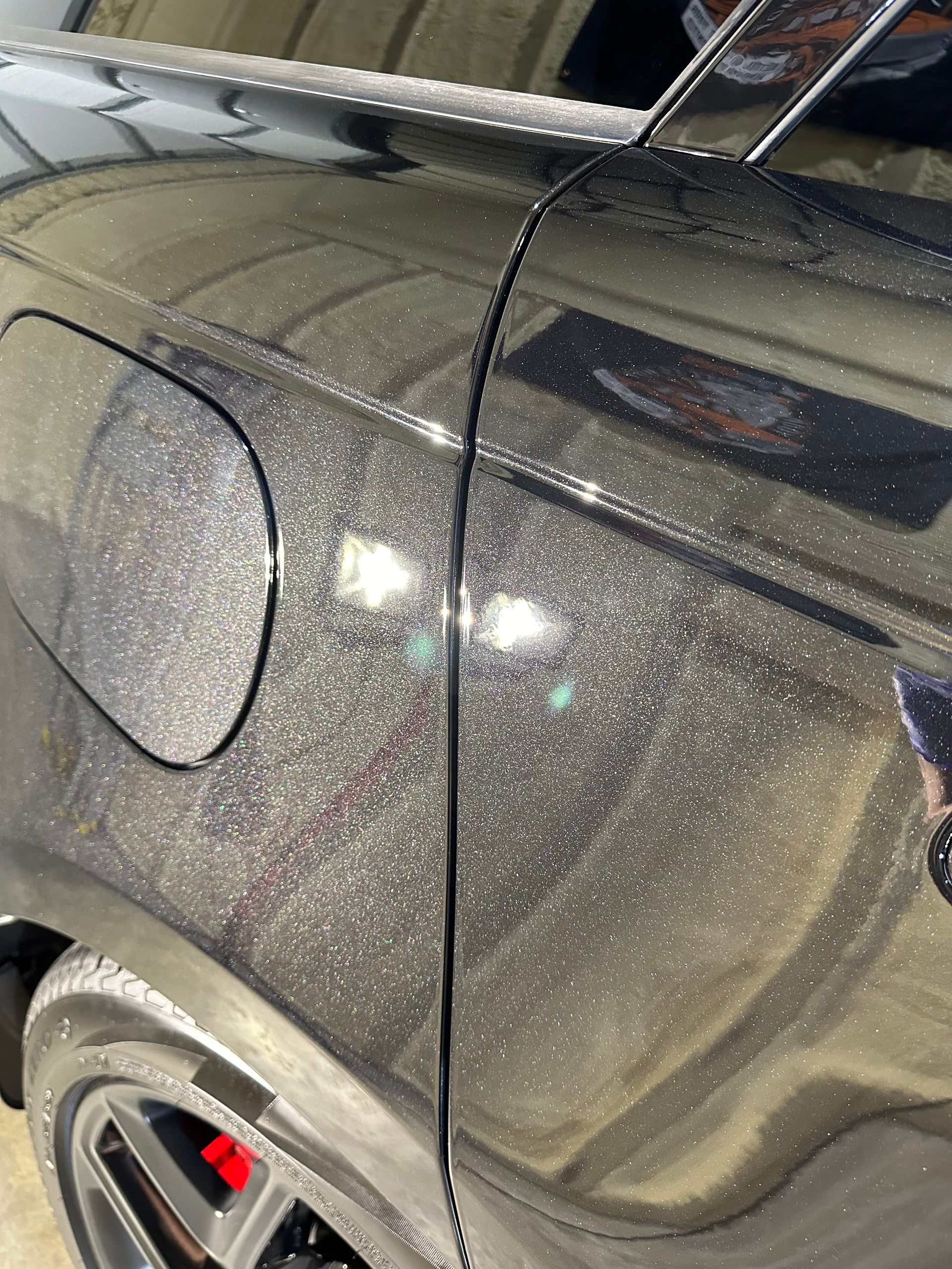 A black car is parked in a garage with a reflection of a building in the door.