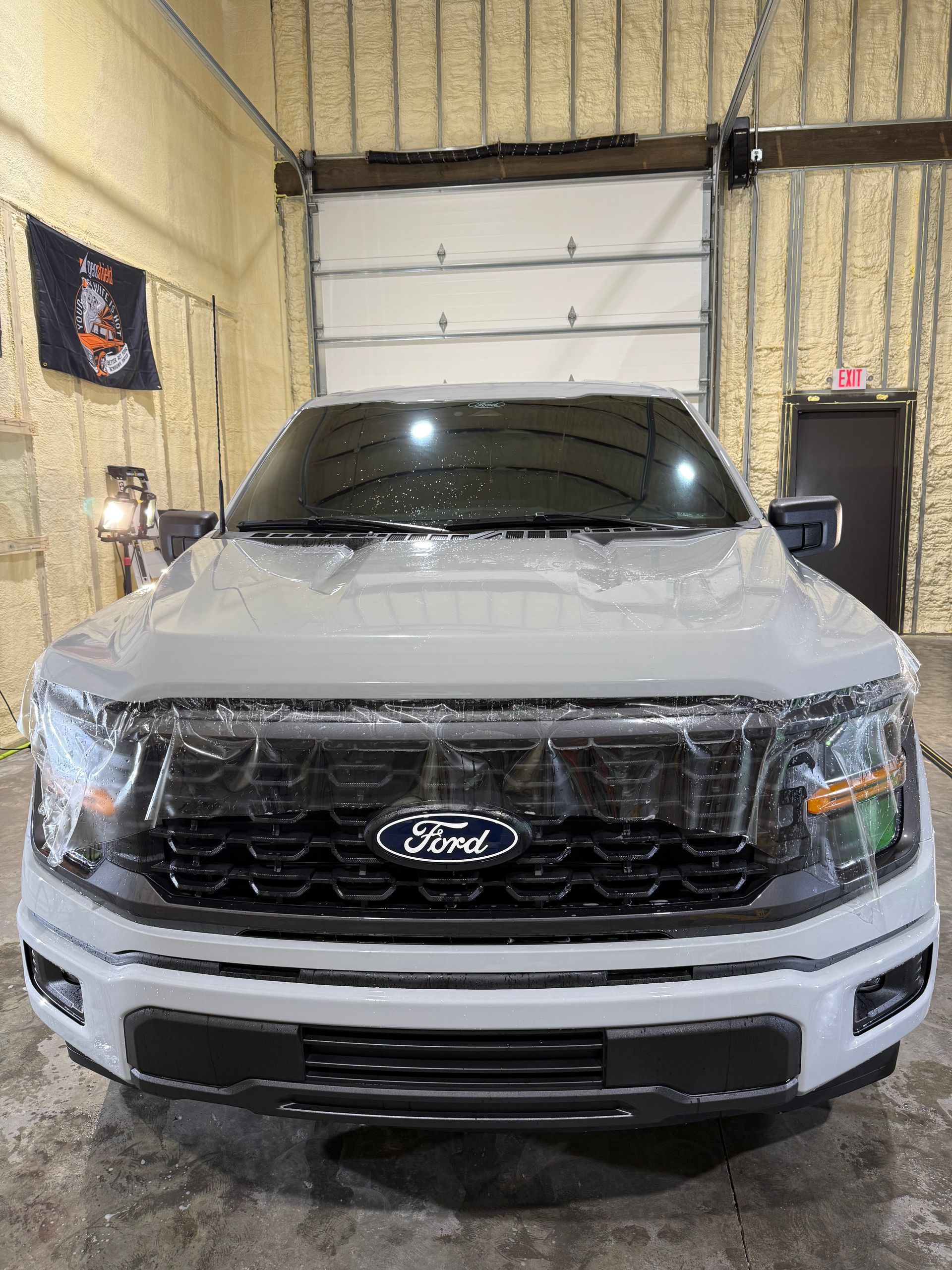 A white ford f150 truck is sitting in a garage covered in plastic.
