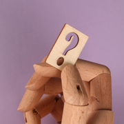 Wooden figurine holding a card with a question mark on a purple background
