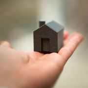 A small black house model resting on an open hand against a blurred background
