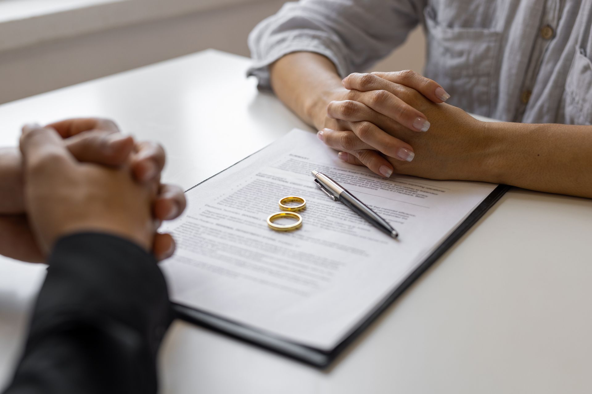 A woman speaks with a divorce lawyer beside a form and two wedding rings on the table.