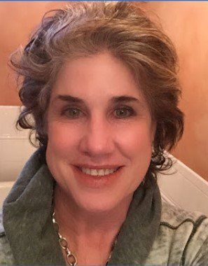 Signs divorce papers — Elkhart Lake, WI — Pro Se Divorce & Mediation Services S.C. Woman with graying curly hair smiles, wearing a green hooded top and silver necklace.