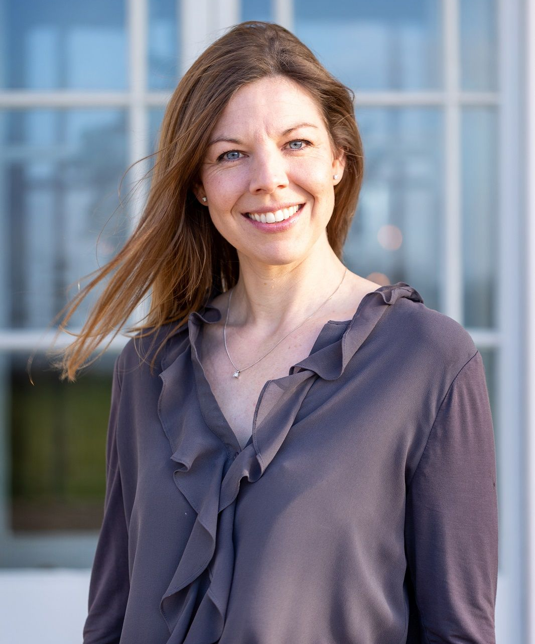 a woman in a ruffled shirt is smiling in front of a window .