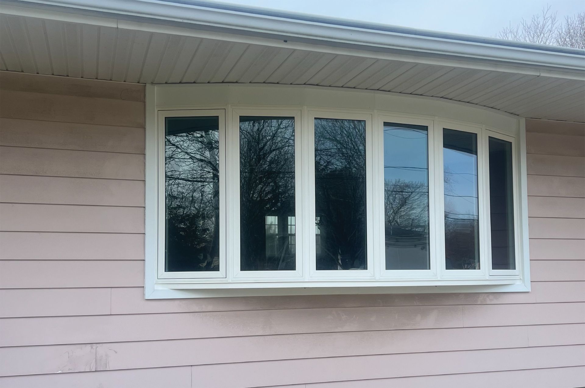 White framed bay window on a pink house with reflections of trees in the glass.