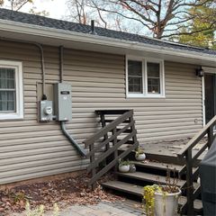 Beige siding of a house with a gray electrical box. A wooden deck and steps are in front of the house.