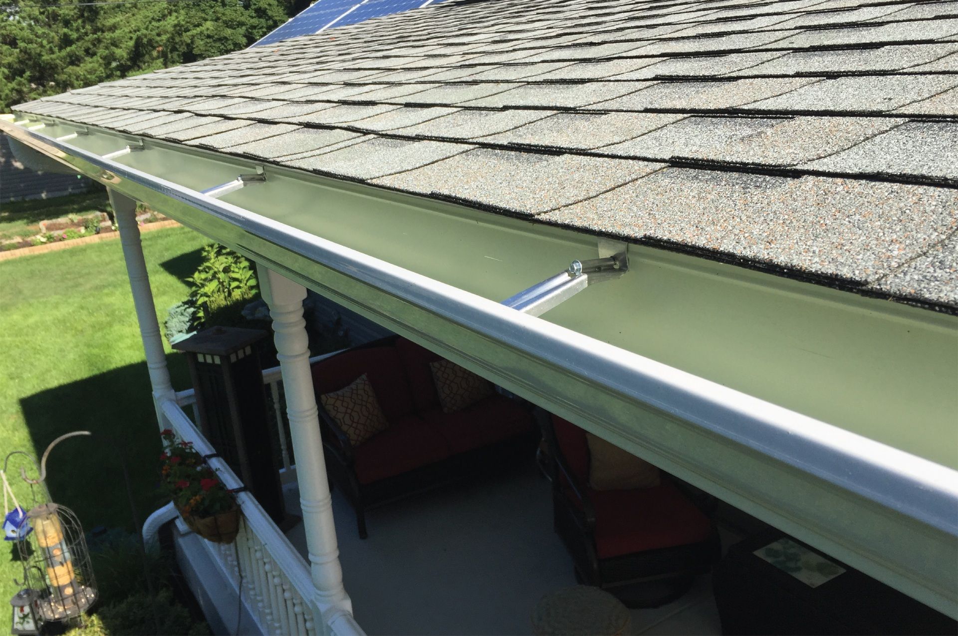 Green gutters with white trim installed along a roofline, over a porch with outdoor seating.