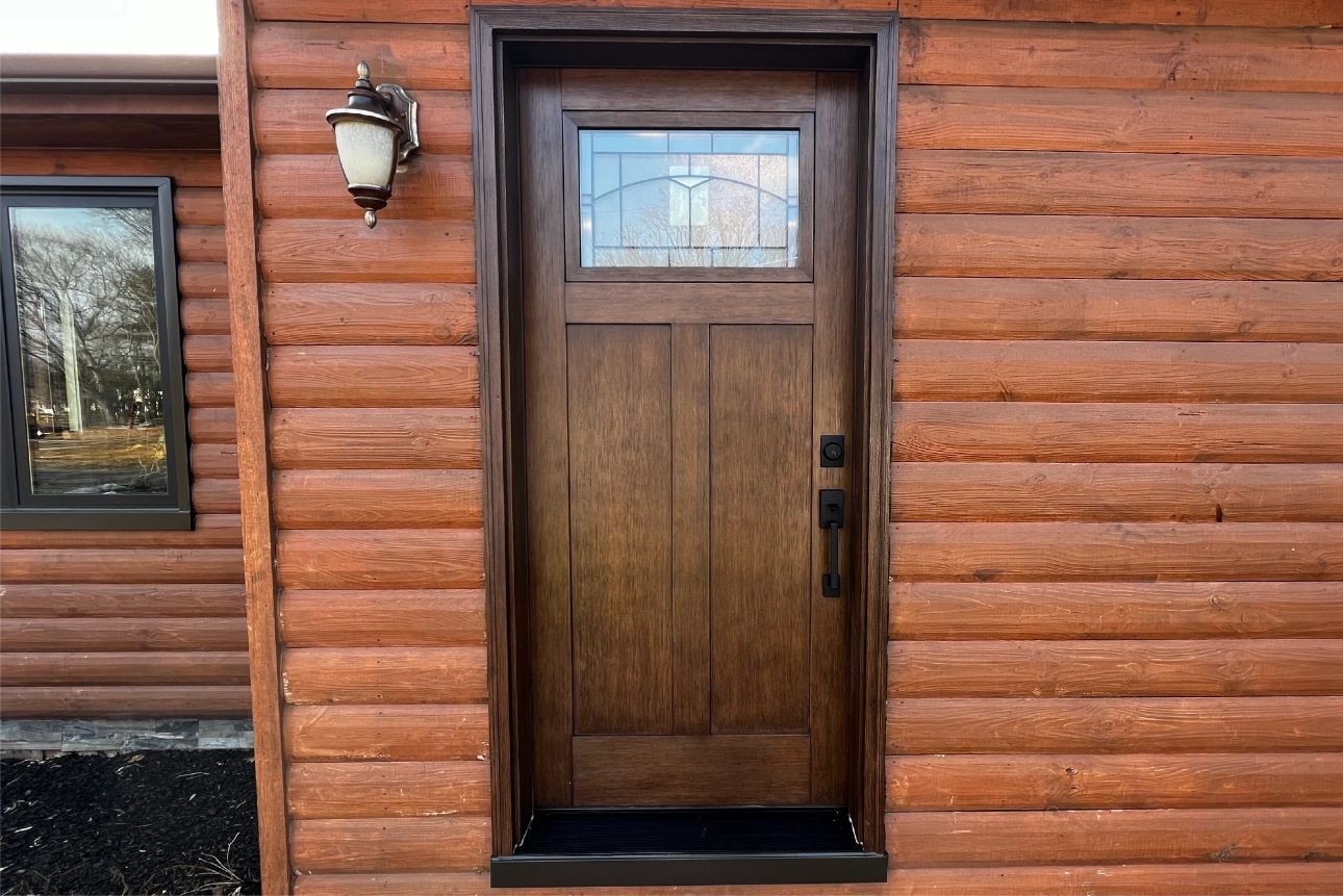 Brown wooden door with glass pane, set in a log cabin style wall, with a light fixture on the side.