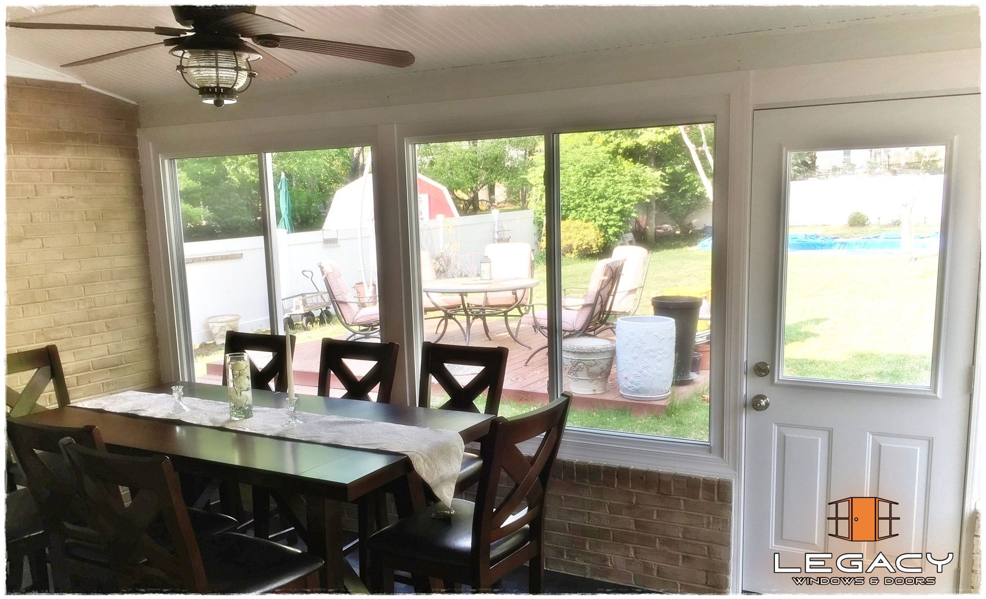 Sunroom interior with dining table, windows overlooking backyard with patio furniture and a door.