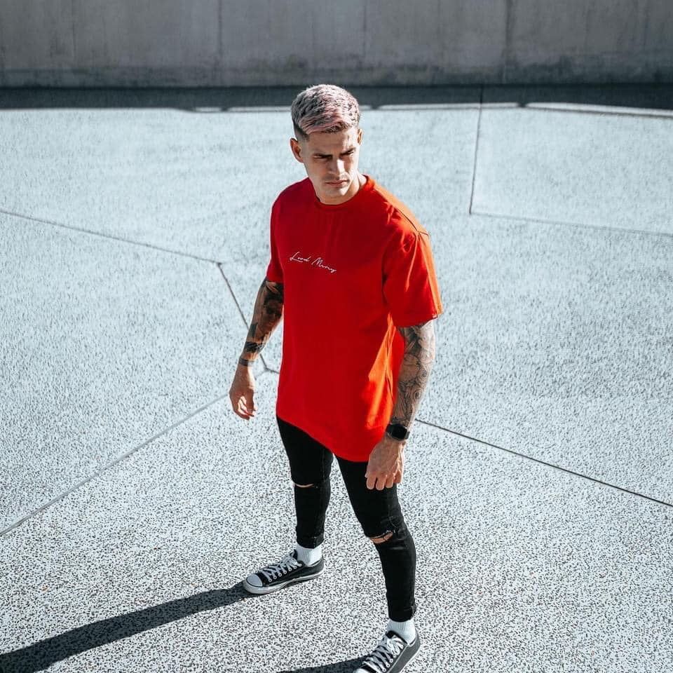A Man Wearing A Red T-shirt And Black Pants Is Standing On A Sidewalk — Carnival Clothing In Miami, QLD