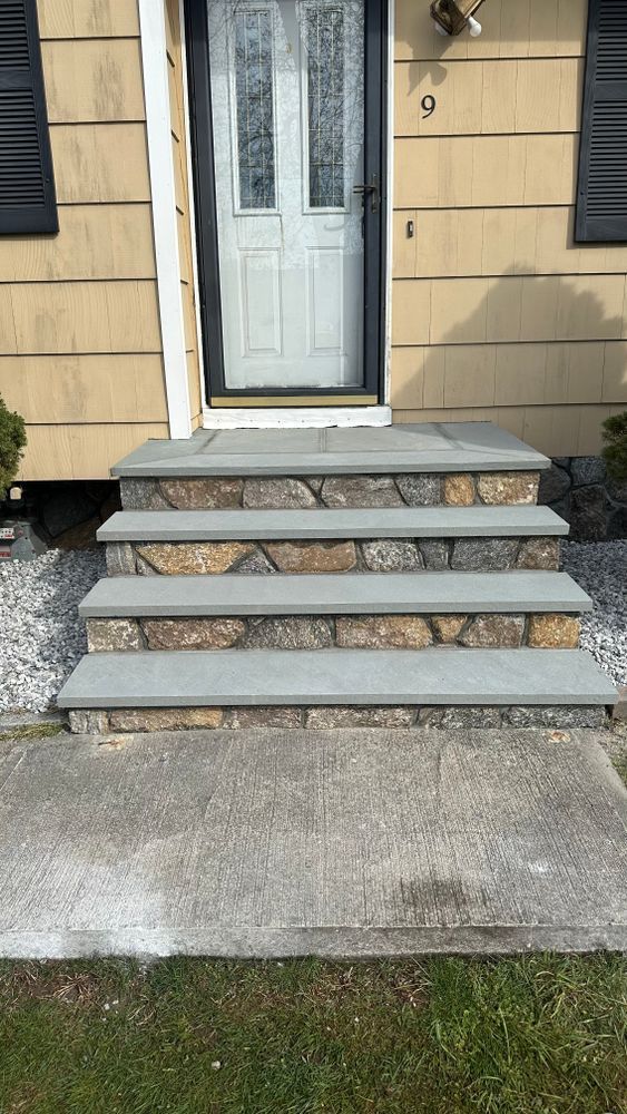 Stone steps leading up to a light-colored front door. The steps have a textured stone front with gray flagstone treads.