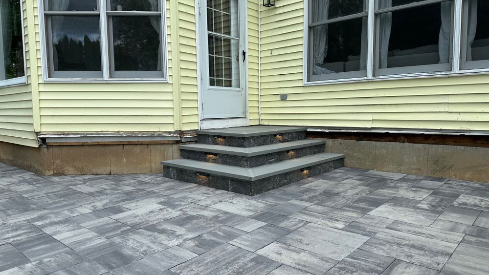 Stone steps leading to a white door on a yellow house. Grey pavers create the patio.