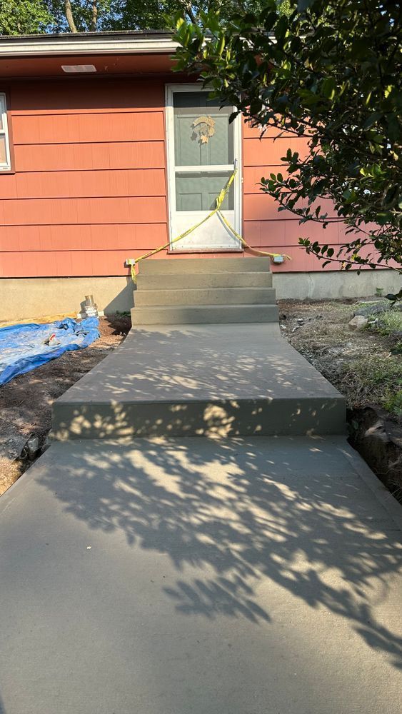 Freshly poured concrete walkway leading to a house with coral-colored siding and a white door, caution tape blocking access.