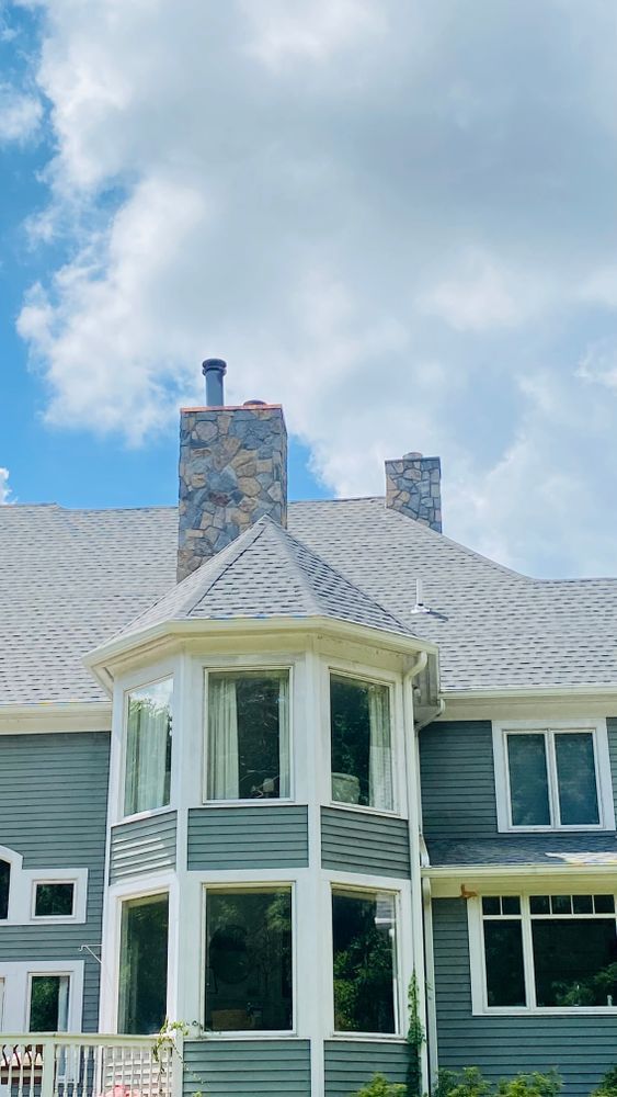 Gray house with a stone chimney against a partly cloudy blue sky.