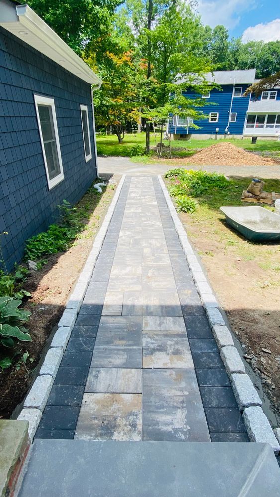 A newly paved walkway with gray and black pavers leads from a blue building.