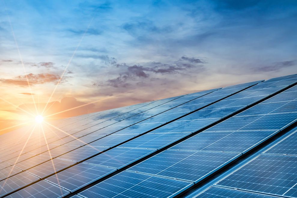 Solar panels at sunrise under a blue sky, reflecting warm sunlight