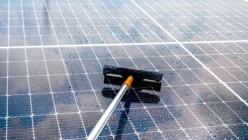 Squeegee cleaning wet solar panels under a sprinkler spray