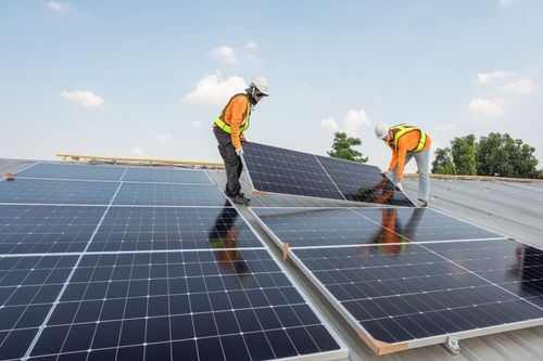 Workers installing solar panels on a rooftop under a clear blue sky.