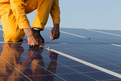 Worker in yellow overalls installing solar panels on a rooftop.