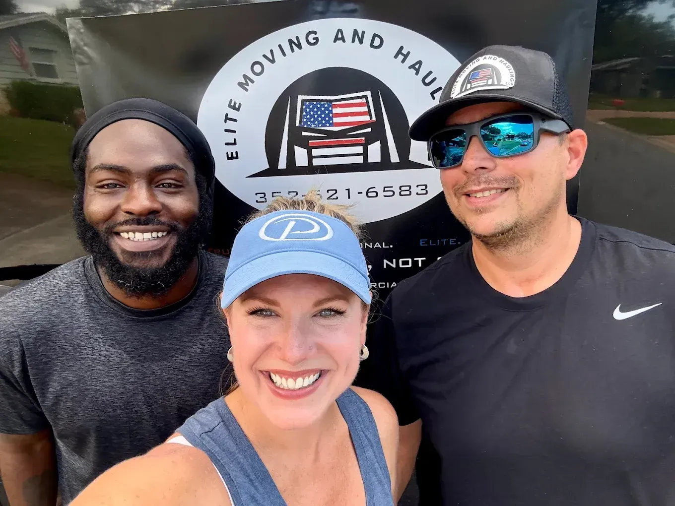 Three smiling people in front of a moving truck with a company logo.