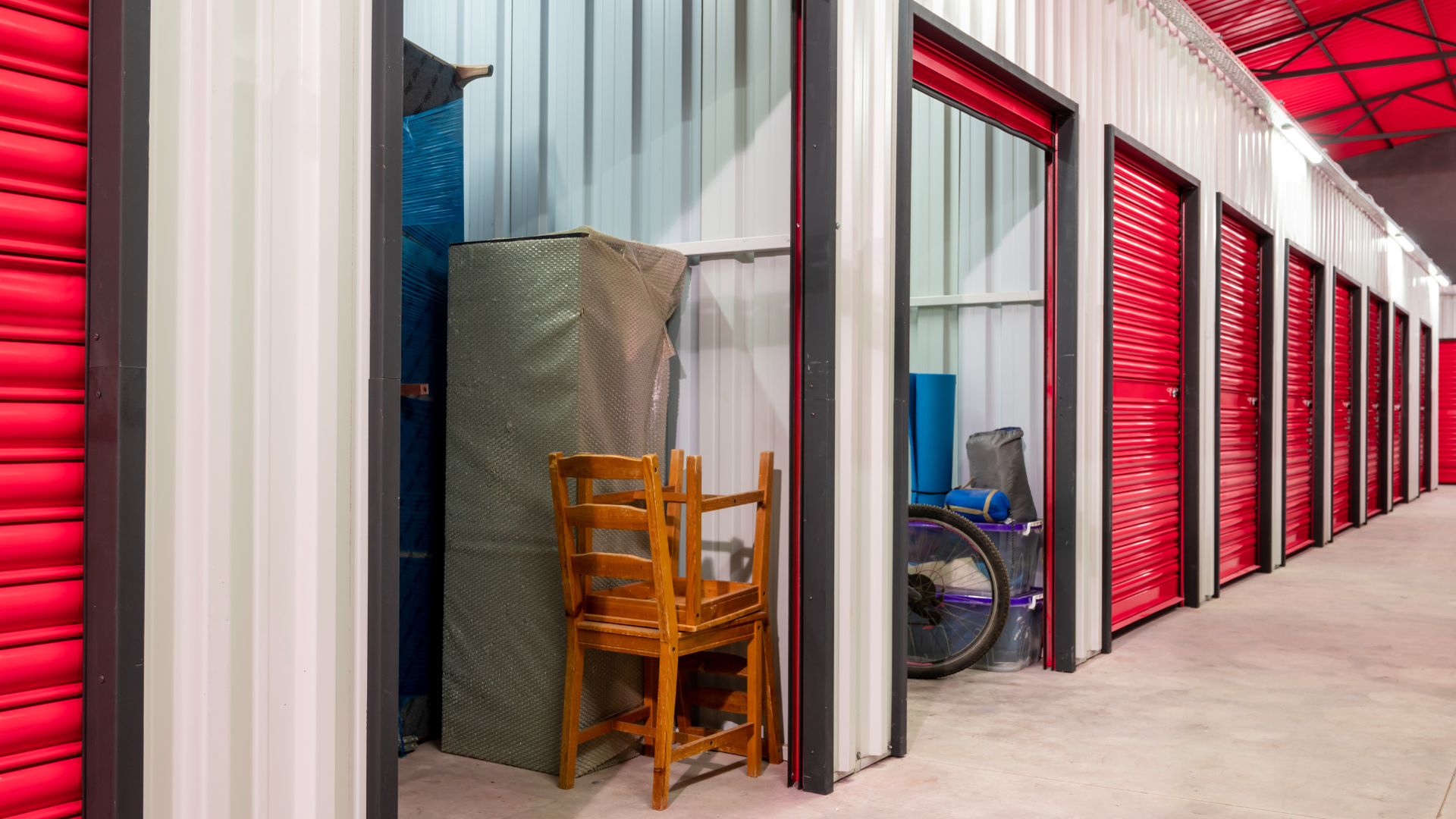 Row of storage units, mostly red doors, some open, revealing stored items.