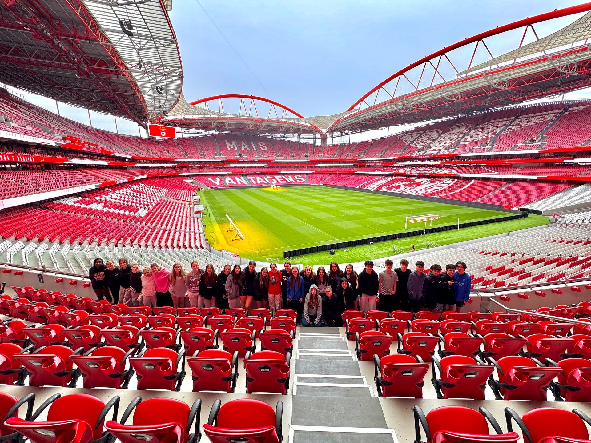 Wide view of a red-seated soccer stadium with a green field and fans in the stands