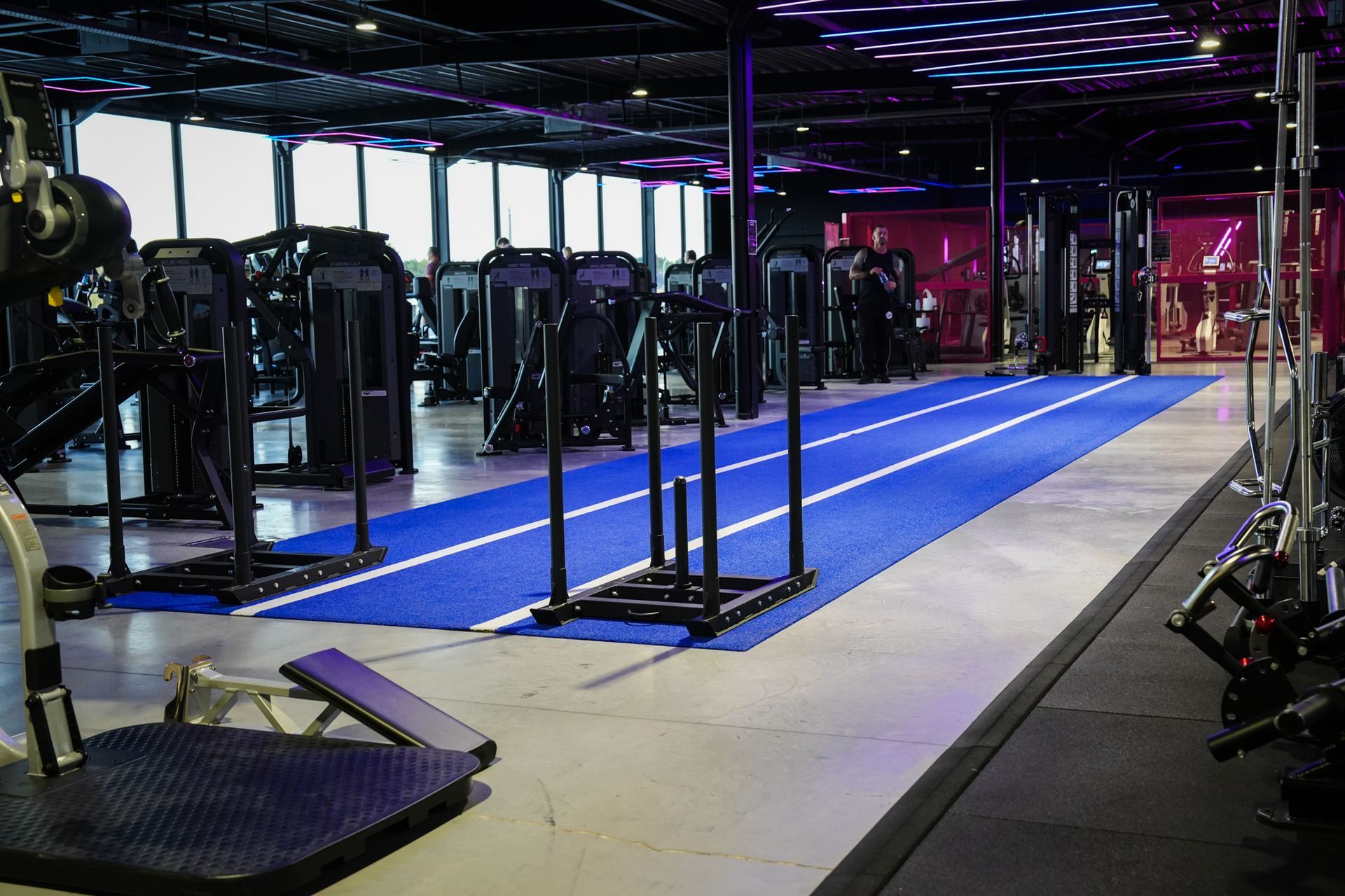 Een sportschool vol met fitnessapparatuur en een blauwe mat.