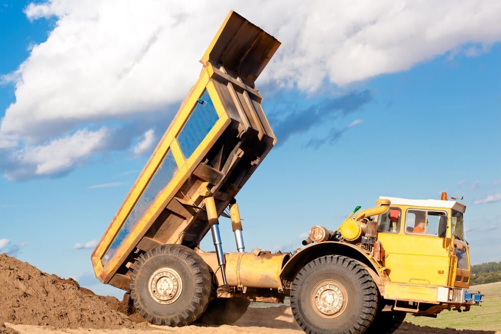 A Yellow Dump Truck Is Dumping Dirt Into A Pile — Dicko's Bobcat & Tipper in East Bendigo, VIC