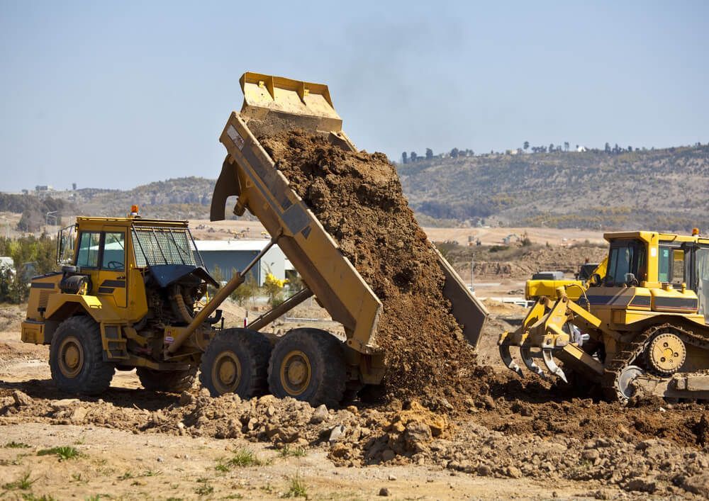 A Dump Truck Is Unloading Dirt On A Dirt Field — Dicko's Bobcat & Tipper in East Bendigo, VIC