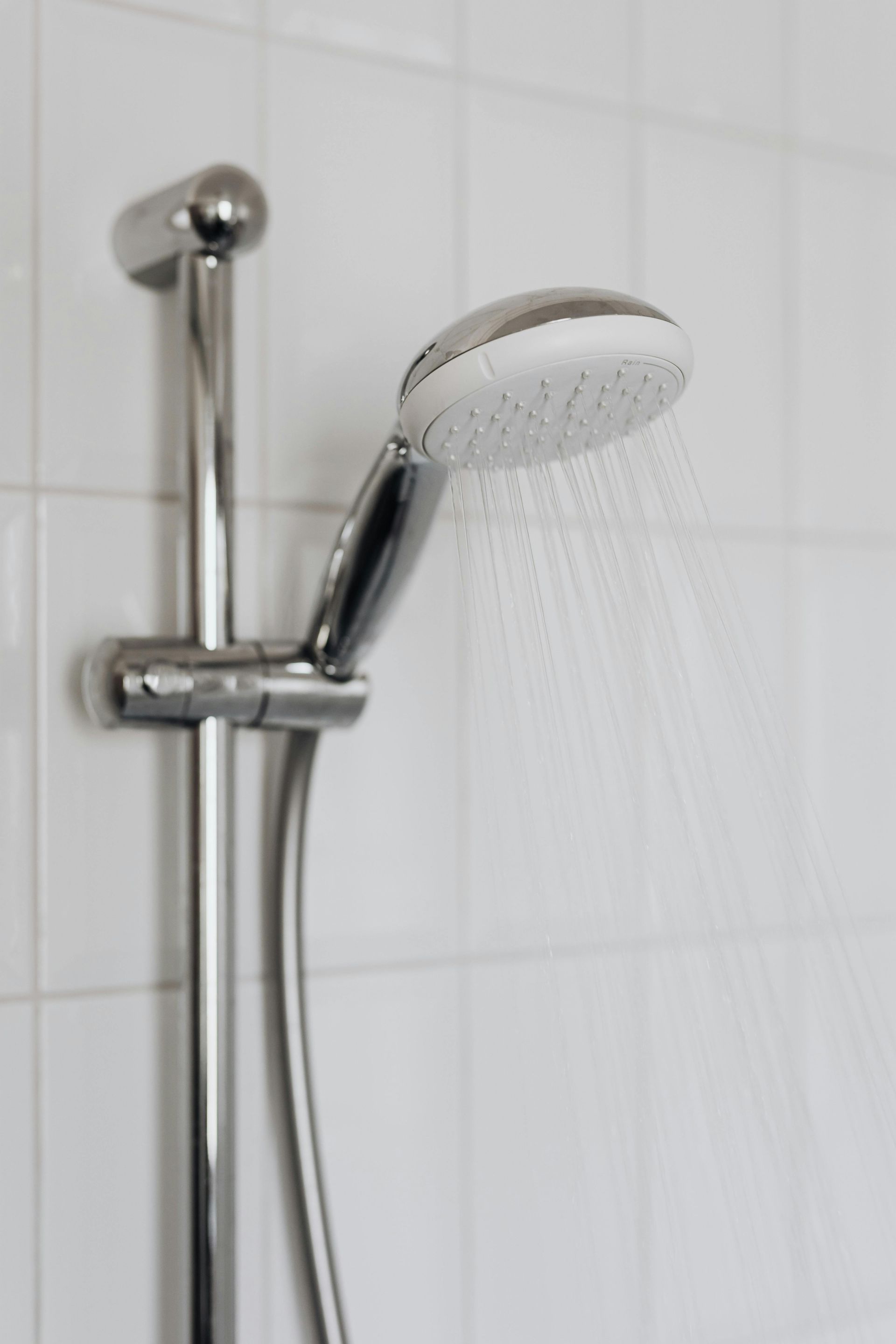 Chrome shower head spraying water against white tiled wall.