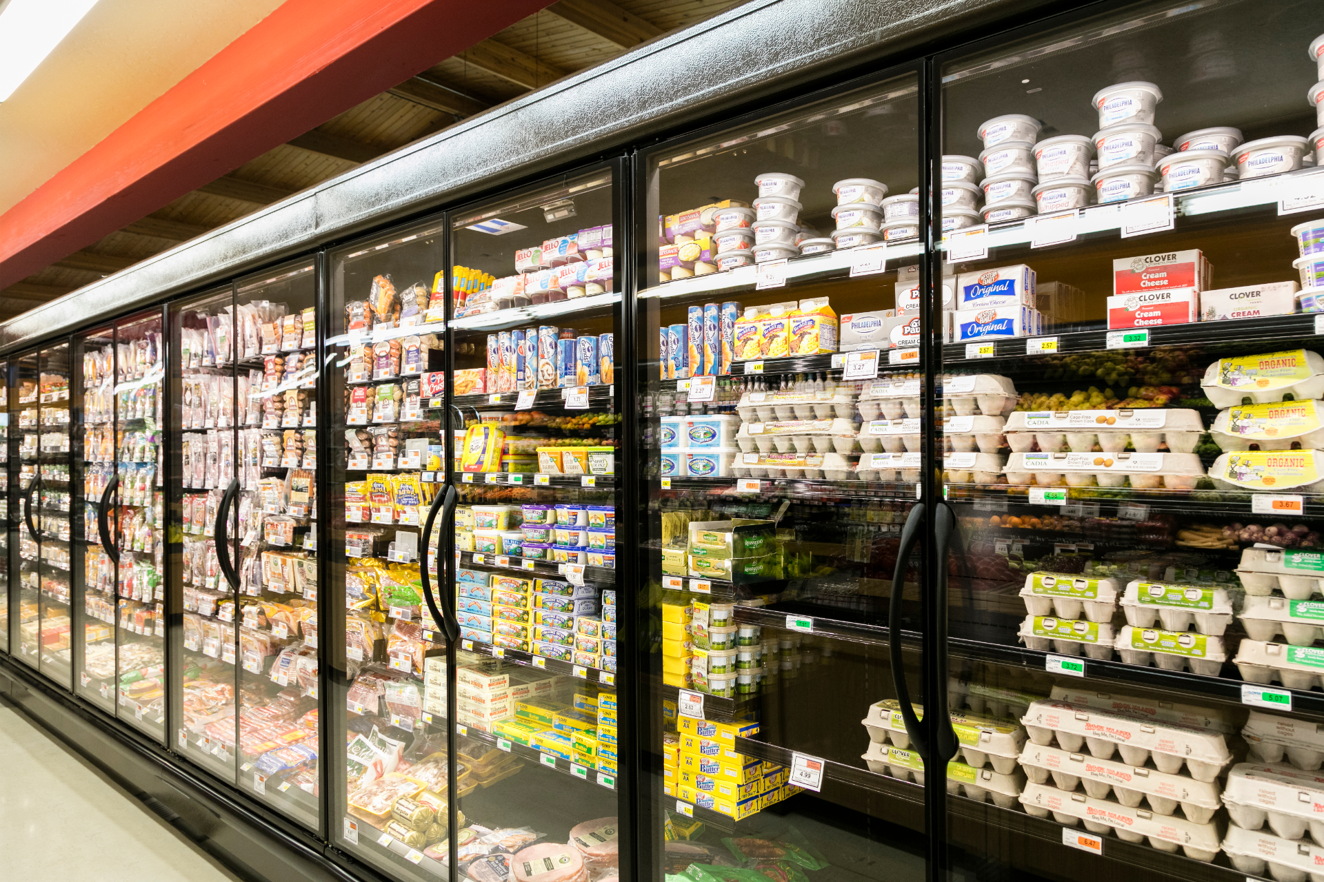 A row of refrigerated grocery store display cases filled with various packaged dairy products, including eggs and yogurt.