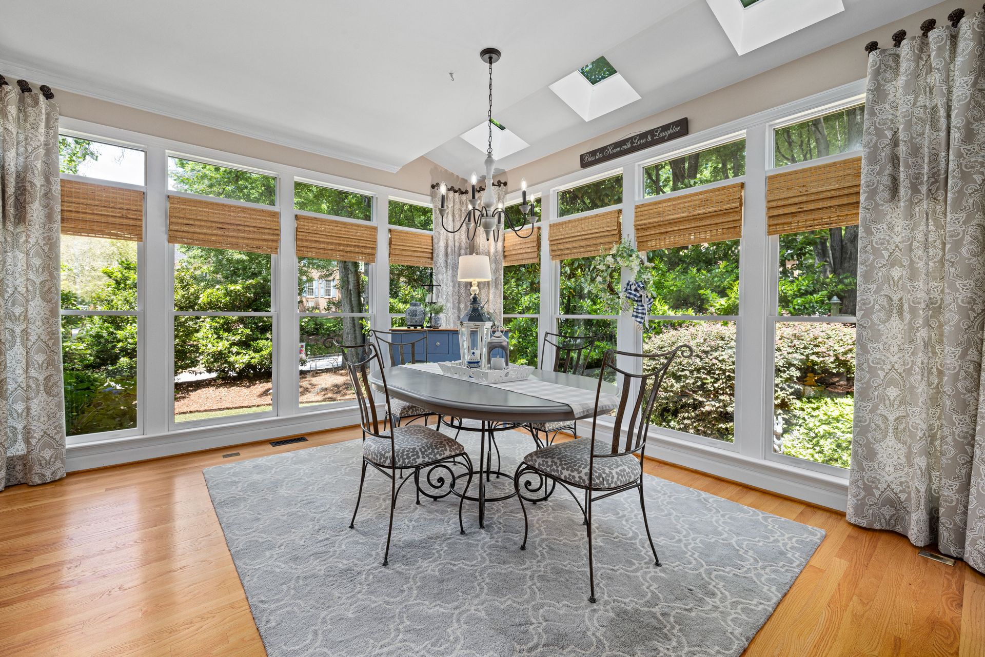 Bright sunroom with large windows, glass dining table, gray rug, and garden views
