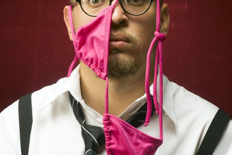 Man wearing glasses and suspenders, with a pink bikini covering half his face, surprised expression.
