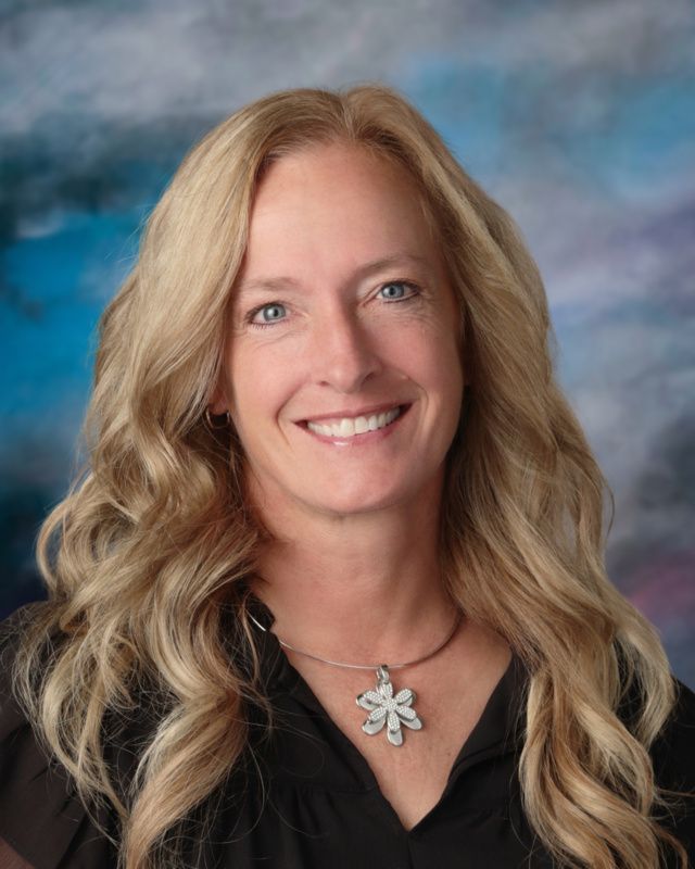 A woman with long blonde hair is smiling for a picture in front of a blue background.