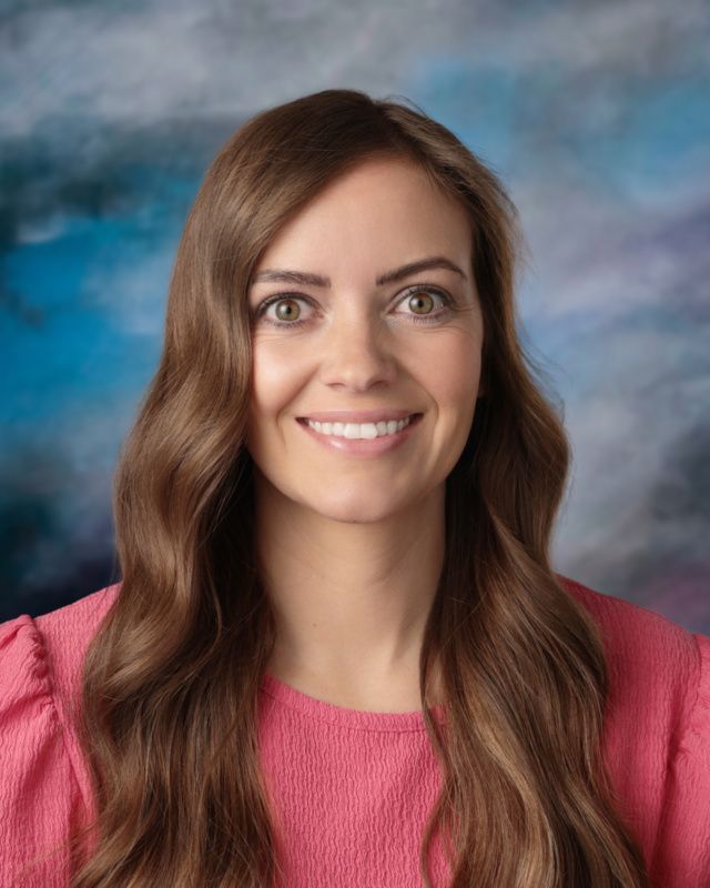 The woman is wearing a pink shirt and smiling for the camera.