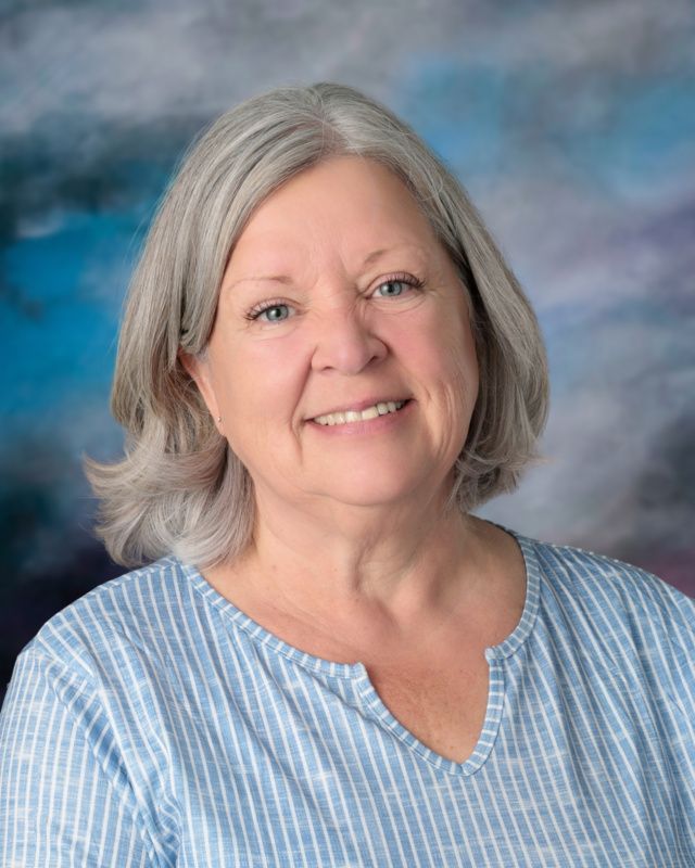 A woman wearing a striped shirt and a necklace is smiling for the camera.