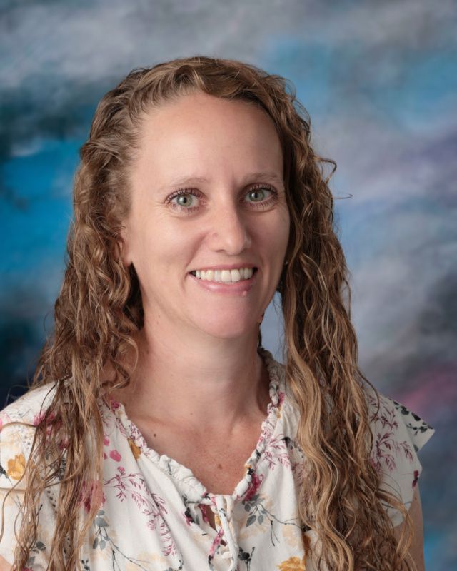 A woman with long curly hair is smiling in front of a blue background.