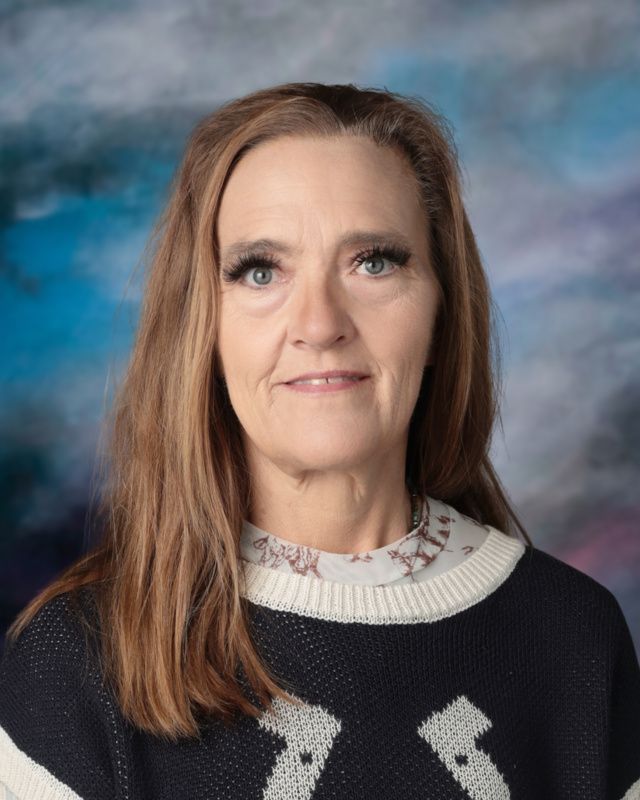 A woman in a floral shirt and necklace is smiling for the camera.