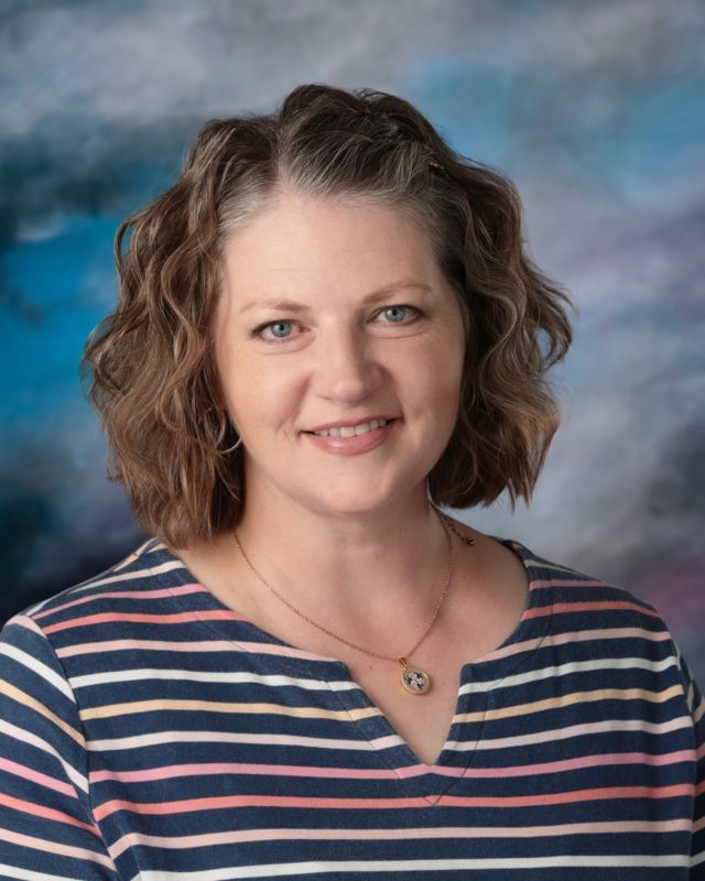 A woman in a floral shirt and necklace is posing for a picture.