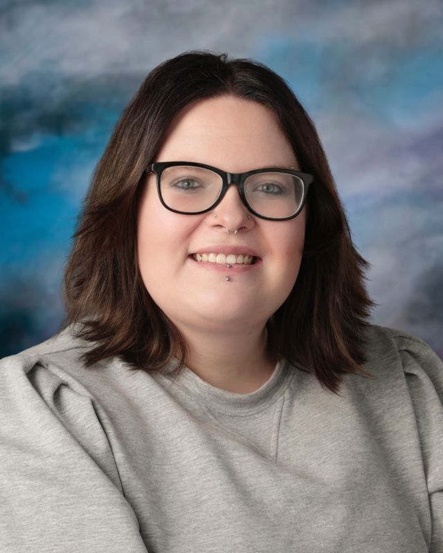 A woman wearing a plaid shirt and a necklace is smiling for the camera.