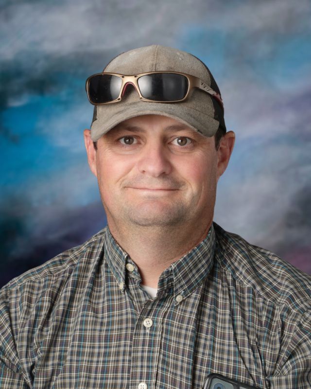 A man wearing a hat and a lanyard is smiling for the camera.