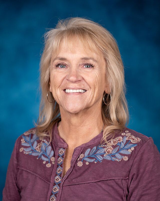 A woman in a purple shirt is smiling in front of a blue background.